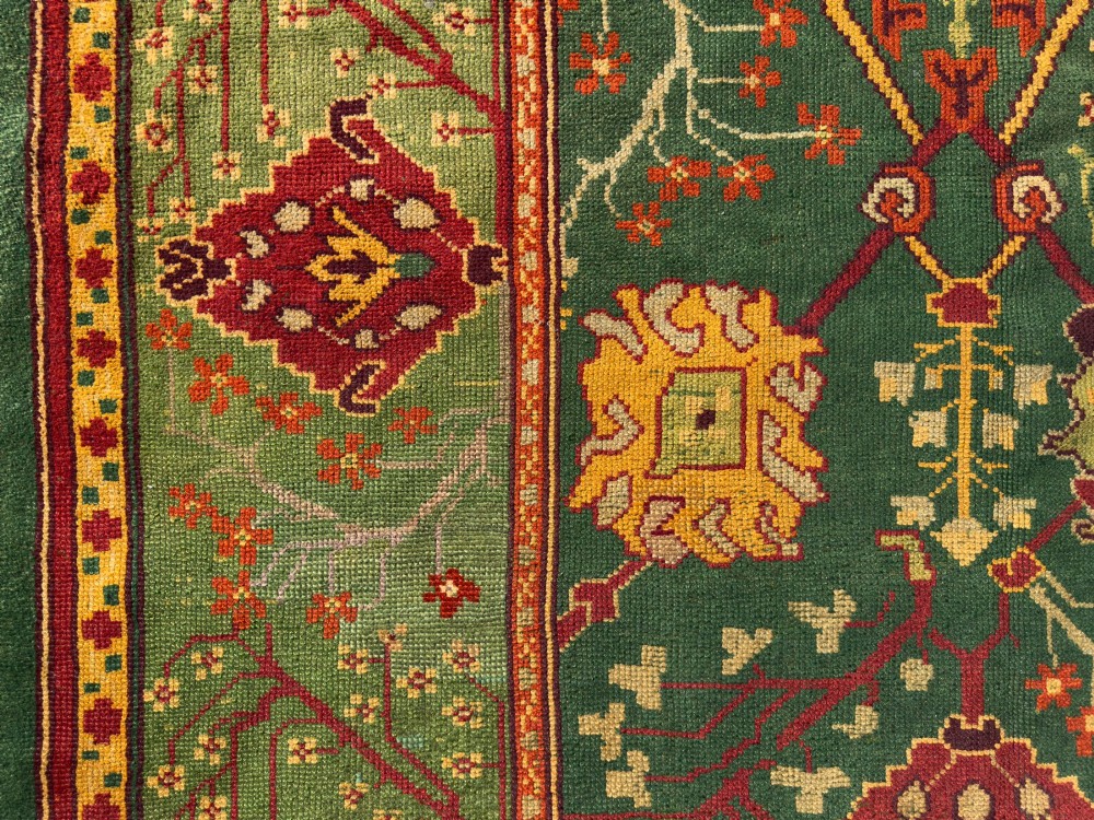 An antique Arts and Crafts hand-knotted wool Donegal carpet featuring a green field filled with stylised red and yellow floral motifs and a decorative geometric border. View VII
