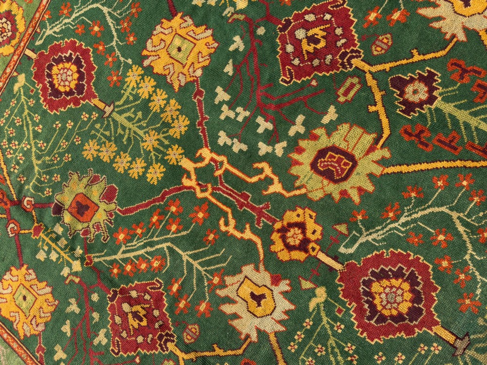 An antique Arts and Crafts hand-knotted wool Donegal carpet featuring a green field filled with stylised red and yellow floral motifs and a decorative geometric border. View IX