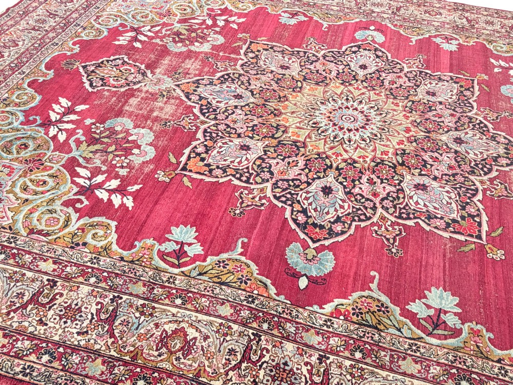 An antique hand-knotted Kirman wool carpet featuring a large central starburst medallion surrounded by floral borders on a crimson red field with distressed wear. View II