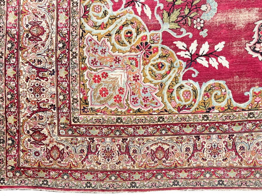 An antique hand-knotted Kirman wool carpet featuring a large central starburst medallion surrounded by floral borders on a crimson red field with distressed wear. View III