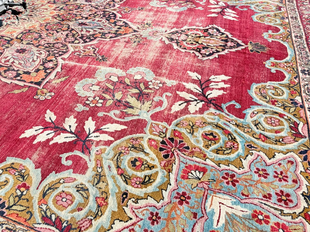 An antique hand-knotted Kirman wool carpet featuring a large central starburst medallion surrounded by floral borders on a crimson red field with distressed wear. View IV