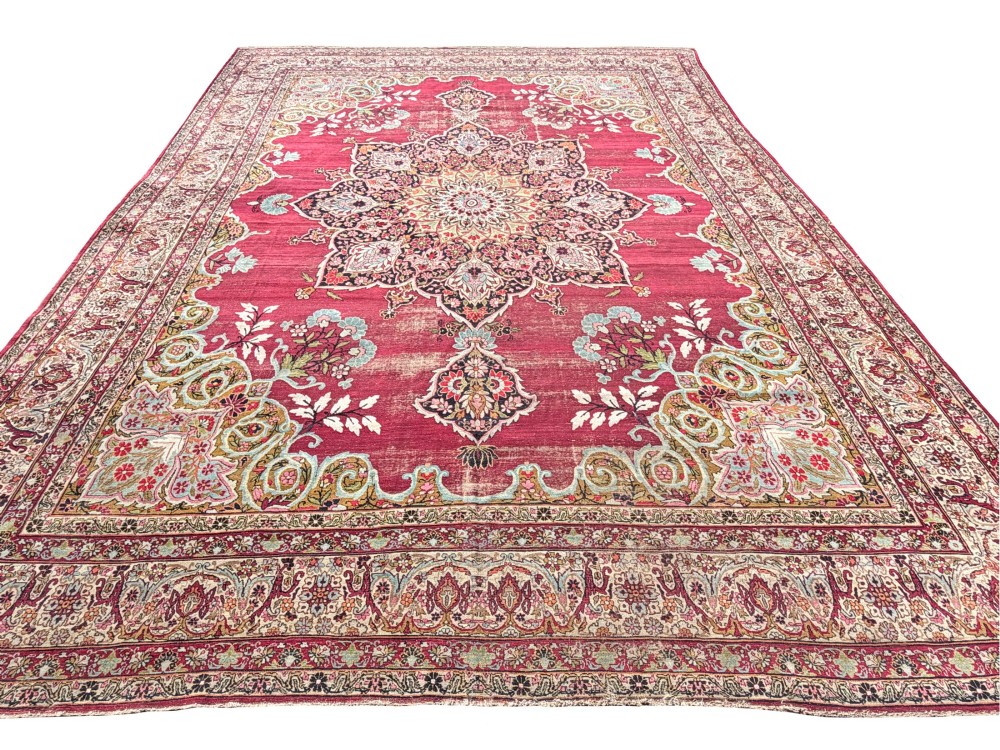 An antique hand-knotted Kirman wool carpet featuring a large central starburst medallion surrounded by floral borders on a crimson red field with distressed wear. View V