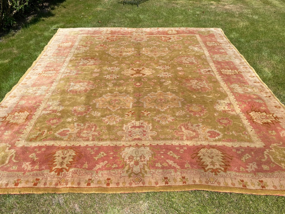 An antique woven wool Ushak carpet featuring a soft olive green field with central palmette motifs surrounded by a pink floral border. View III