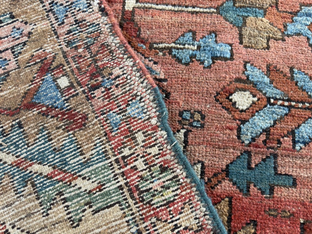 An antique Persian Heriz hand-knotted carpet featuring a terracotta red field filled with geometric motifs, enclosed by a blue and beige patterned border. View III
