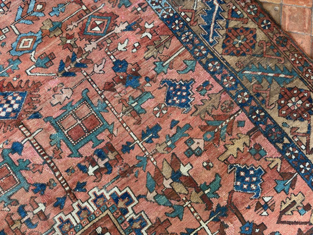 An antique Persian Heriz hand-knotted carpet featuring a terracotta red field filled with geometric motifs, enclosed by a blue and beige patterned border. View IV