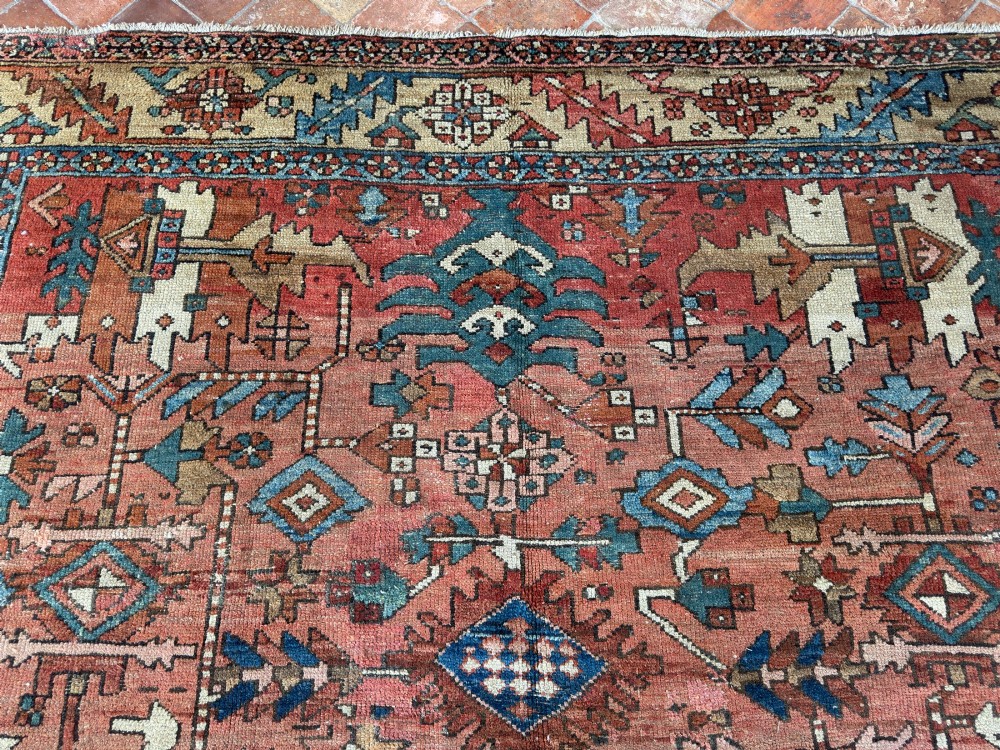 An antique Persian Heriz hand-knotted carpet featuring a terracotta red field filled with geometric motifs, enclosed by a blue and beige patterned border. View V