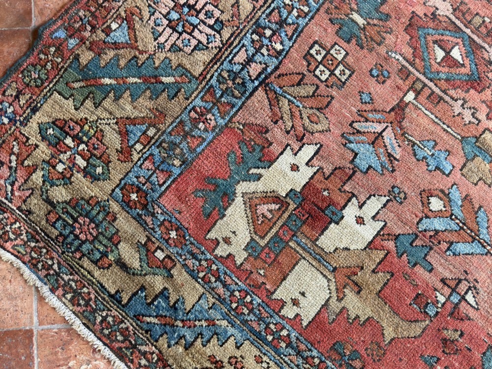 An antique Persian Heriz hand-knotted carpet featuring a terracotta red field filled with geometric motifs, enclosed by a blue and beige patterned border. View VI