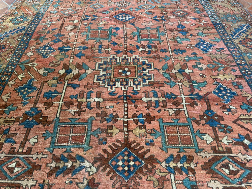 An antique Persian Heriz hand-knotted carpet featuring a terracotta red field filled with geometric motifs, enclosed by a blue and beige patterned border. View VII