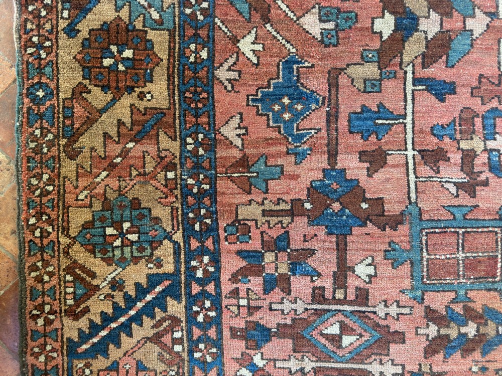 An antique Persian Heriz hand-knotted carpet featuring a terracotta red field filled with geometric motifs, enclosed by a blue and beige patterned border. View VIII