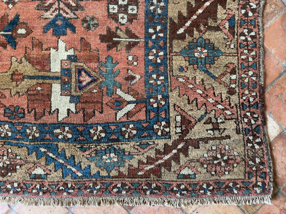 An antique Persian Heriz hand-knotted carpet featuring a terracotta red field filled with geometric motifs, enclosed by a blue and beige patterned border. View IX