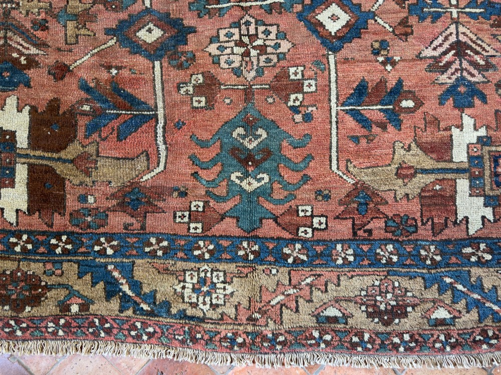 An antique Persian Heriz hand-knotted carpet featuring a terracotta red field filled with geometric motifs, enclosed by a blue and beige patterned border. View X