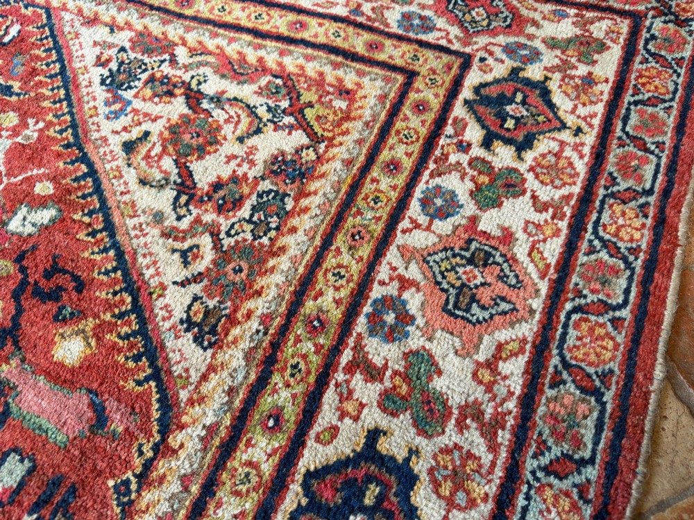 A hand-knotted antique Persian Mahal carpet featuring a terracotta red field with intricate floral motifs surrounded by cream and navy decorative borders. View VI