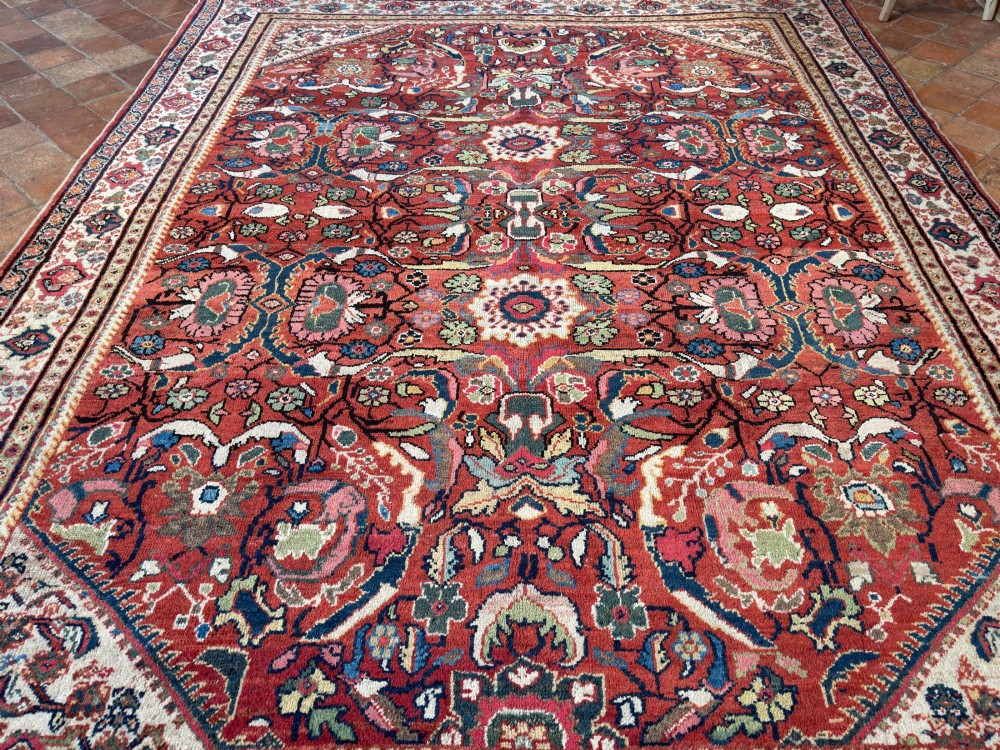 A hand-knotted antique Persian Mahal carpet featuring a terracotta red field with intricate floral motifs surrounded by cream and navy decorative borders. View X