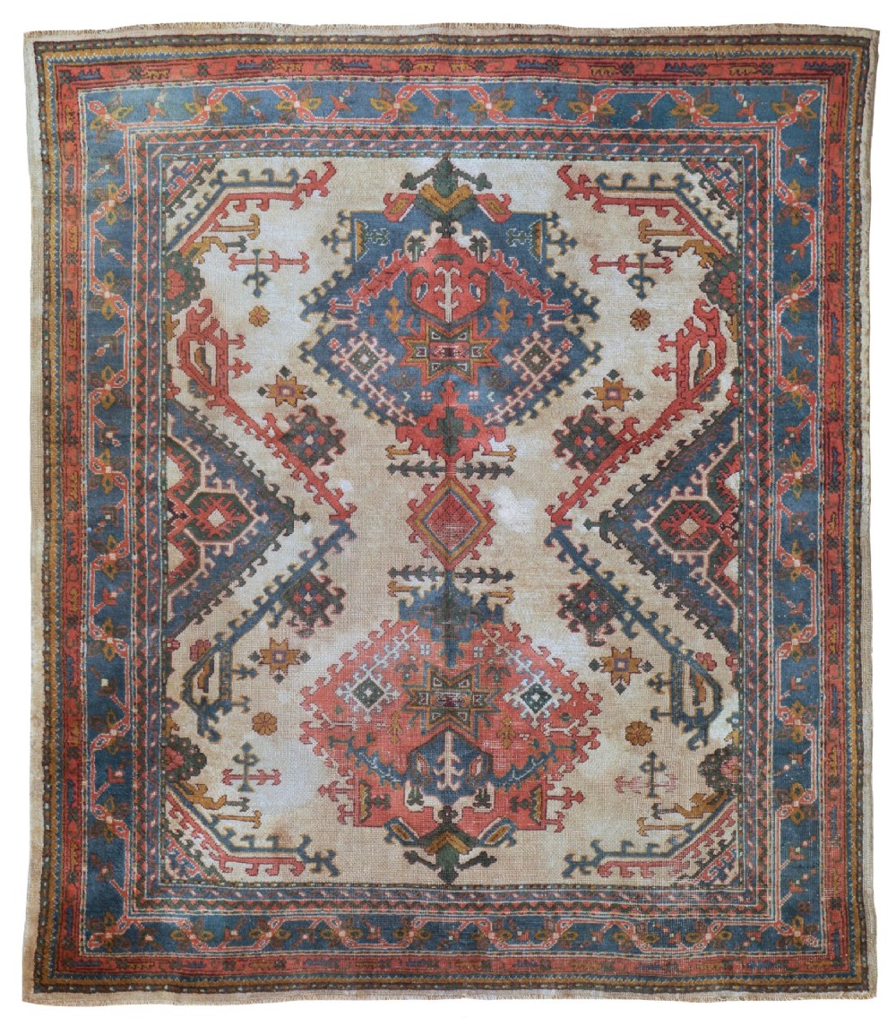 A rectangular hand-knotted wool Ushak carpet featuring central geometric diamond medallions in terracotta red and blue set against a cream field with framed borders.