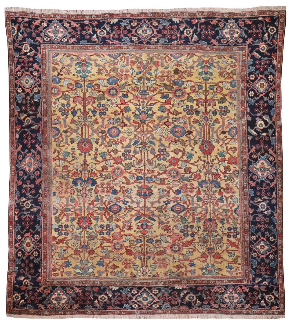 An antique Farahan Persian wool carpet with a yellow floral field framed by a dark navy decorative border.