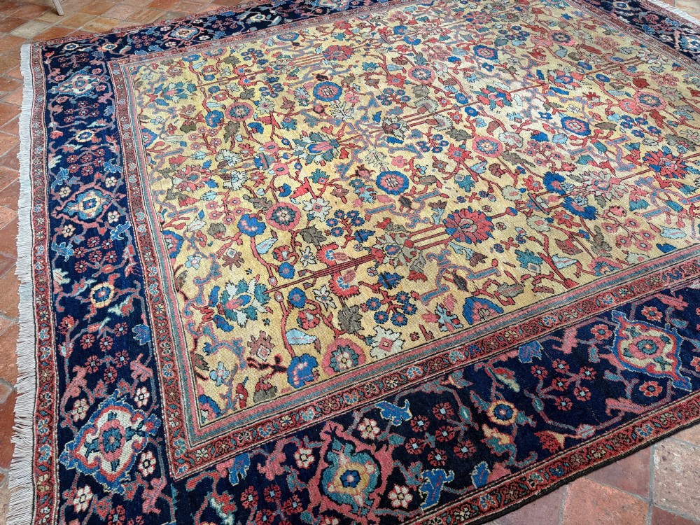 An antique Farahan Persian wool carpet with a yellow floral field framed by a dark navy decorative border. View V
