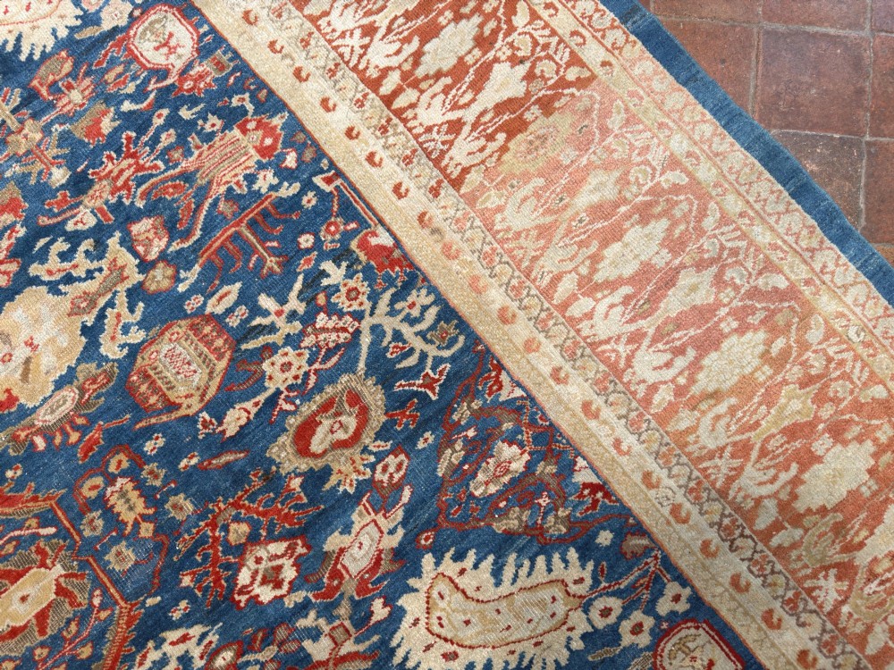 An antique hand-knotted Persian Ziegler carpet featuring a deep indigo blue central field decorated with ivory and terracotta floral motifs inside a wide terracotta border. View II