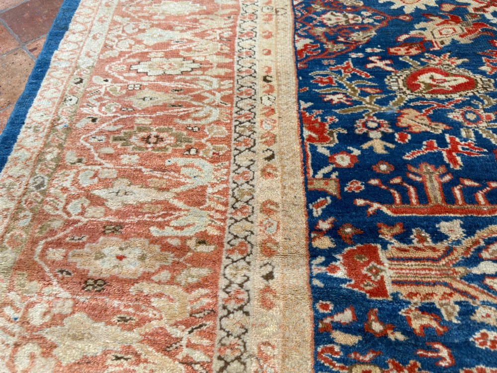 An antique hand-knotted Persian Ziegler carpet featuring a deep indigo blue central field decorated with ivory and terracotta floral motifs inside a wide terracotta border. View V
