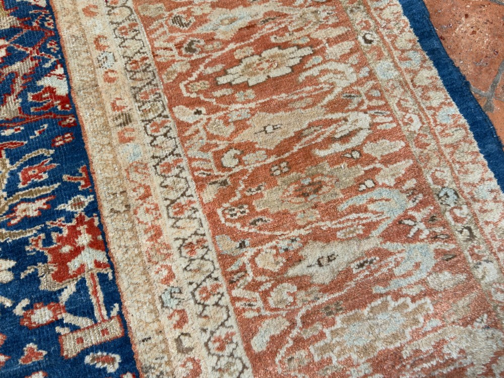 An antique hand-knotted Persian Ziegler carpet featuring a deep indigo blue central field decorated with ivory and terracotta floral motifs inside a wide terracotta border. View VI