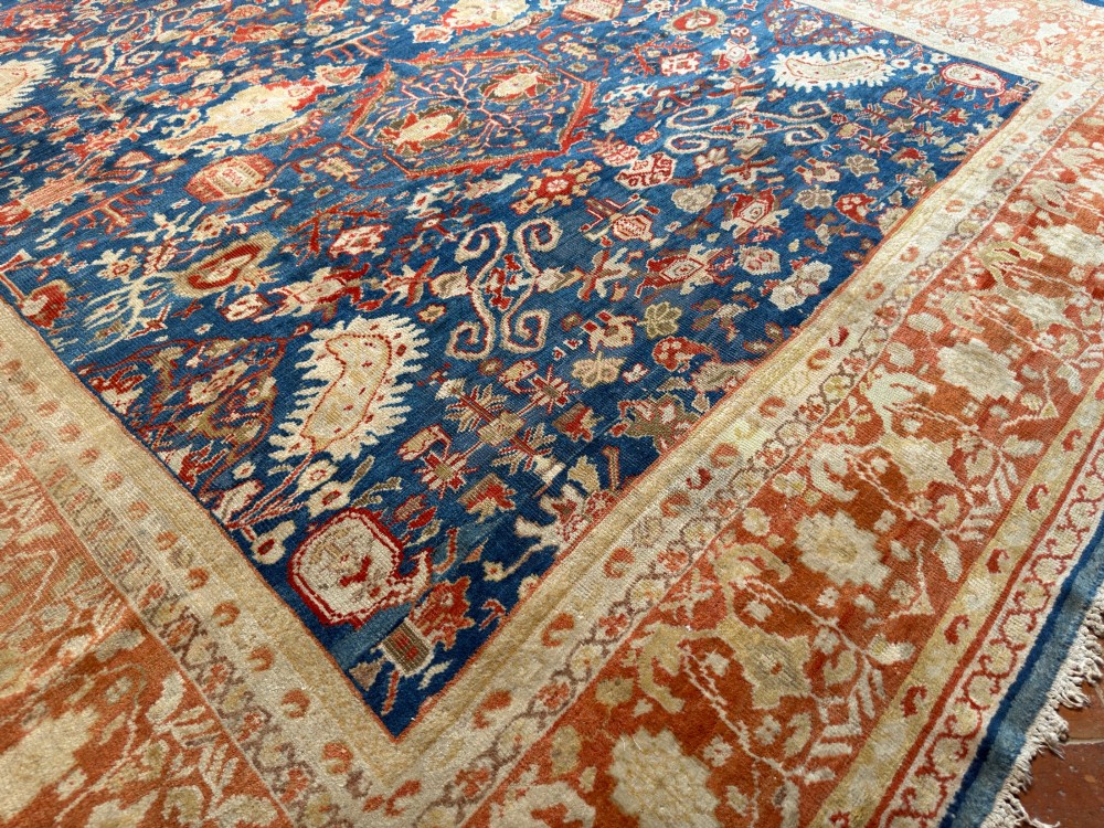 An antique hand-knotted Persian Ziegler carpet featuring a deep indigo blue central field decorated with ivory and terracotta floral motifs inside a wide terracotta border. View VII