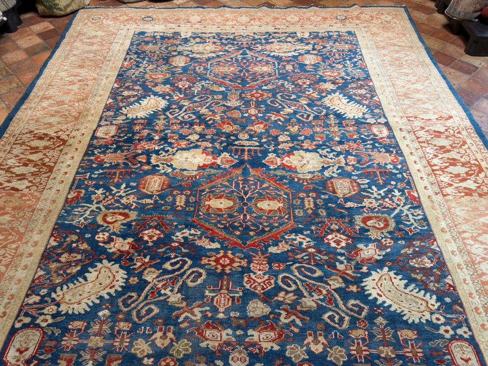 An antique hand-knotted Persian Ziegler carpet featuring a deep indigo blue central field decorated with ivory and terracotta floral motifs inside a wide terracotta border. View X