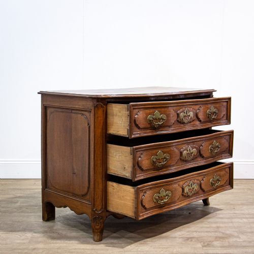 fig 1. An 18th-century French Louis XV oak commode featuring three serpentine drawers with carved moulded panels, ornate brass handles, and carved cabriole legs.