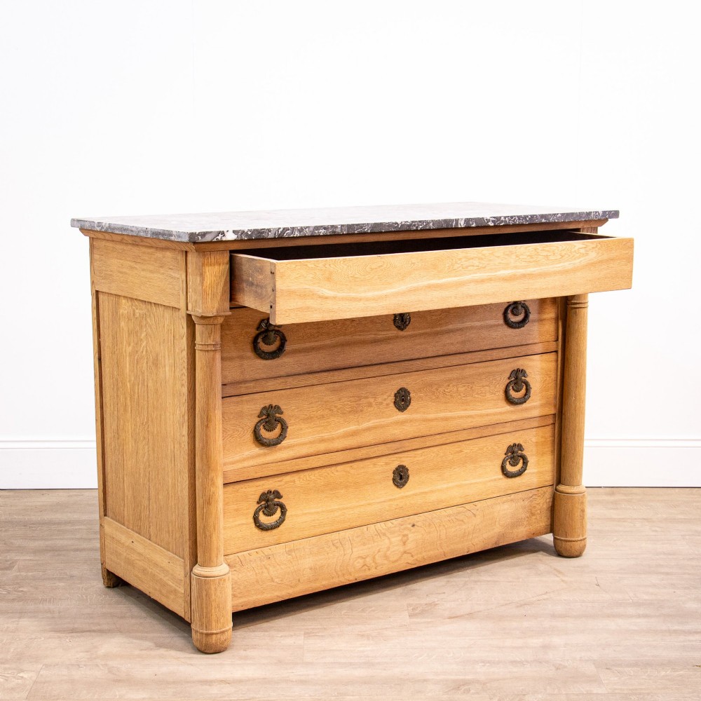 A nineteenth-century bleached oak French Empire commode featuring four drawers, flanking columns, brass ring pull handles, and a dark grey marble top. View III
