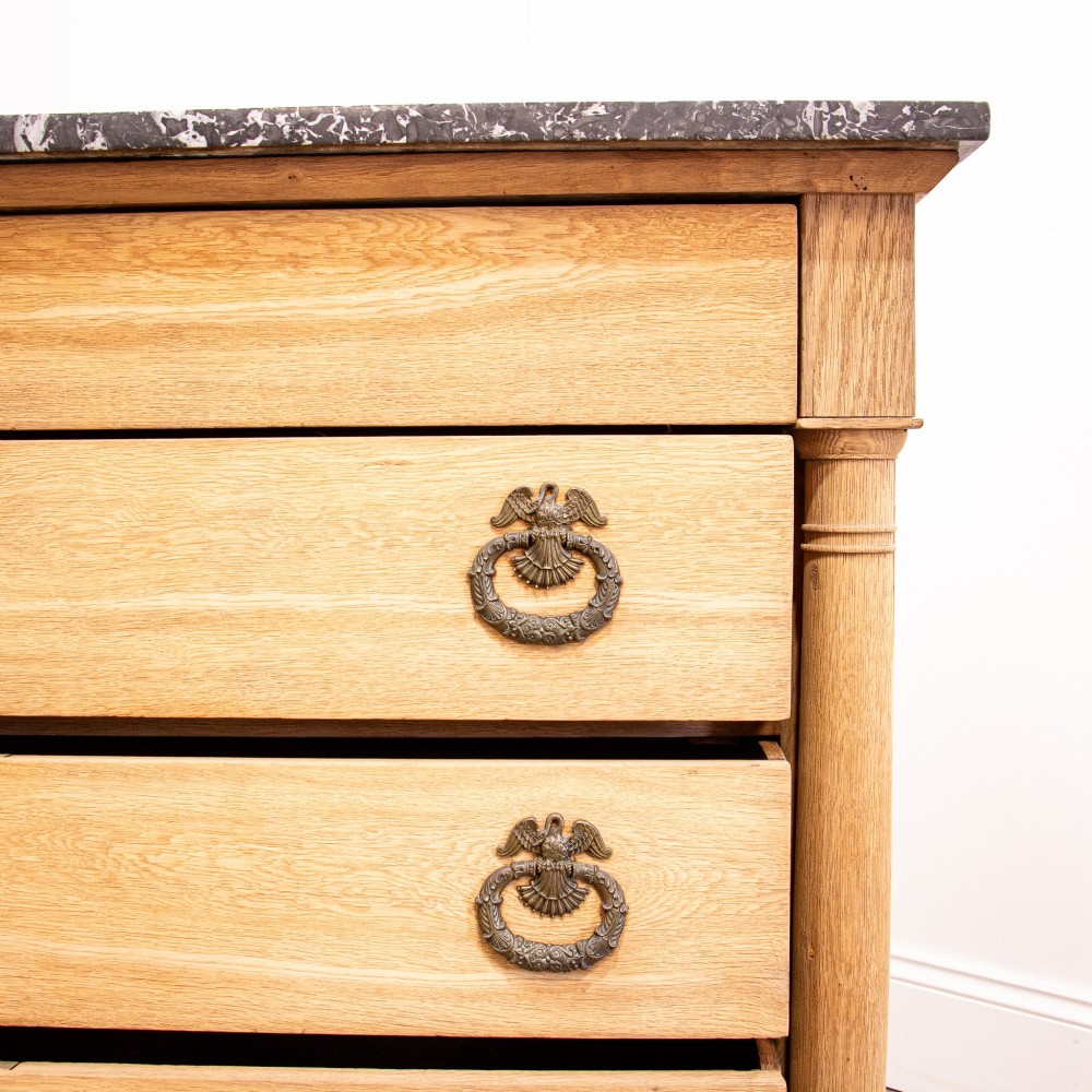 A nineteenth-century bleached oak French Empire commode featuring four drawers, flanking columns, brass ring pull handles, and a dark grey marble top. View XI