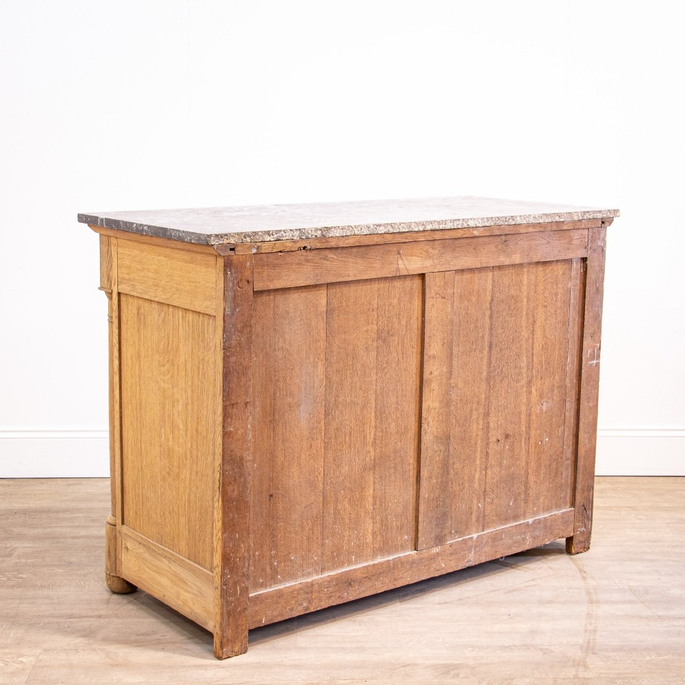 A nineteenth-century bleached oak French Empire commode featuring four drawers, flanking columns, brass ring pull handles, and a dark grey marble top. View XIV