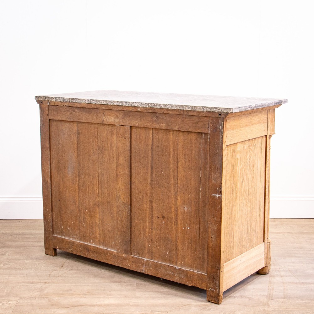 A nineteenth-century bleached oak French Empire commode featuring four drawers, flanking columns, brass ring pull handles, and a dark grey marble top. View XV