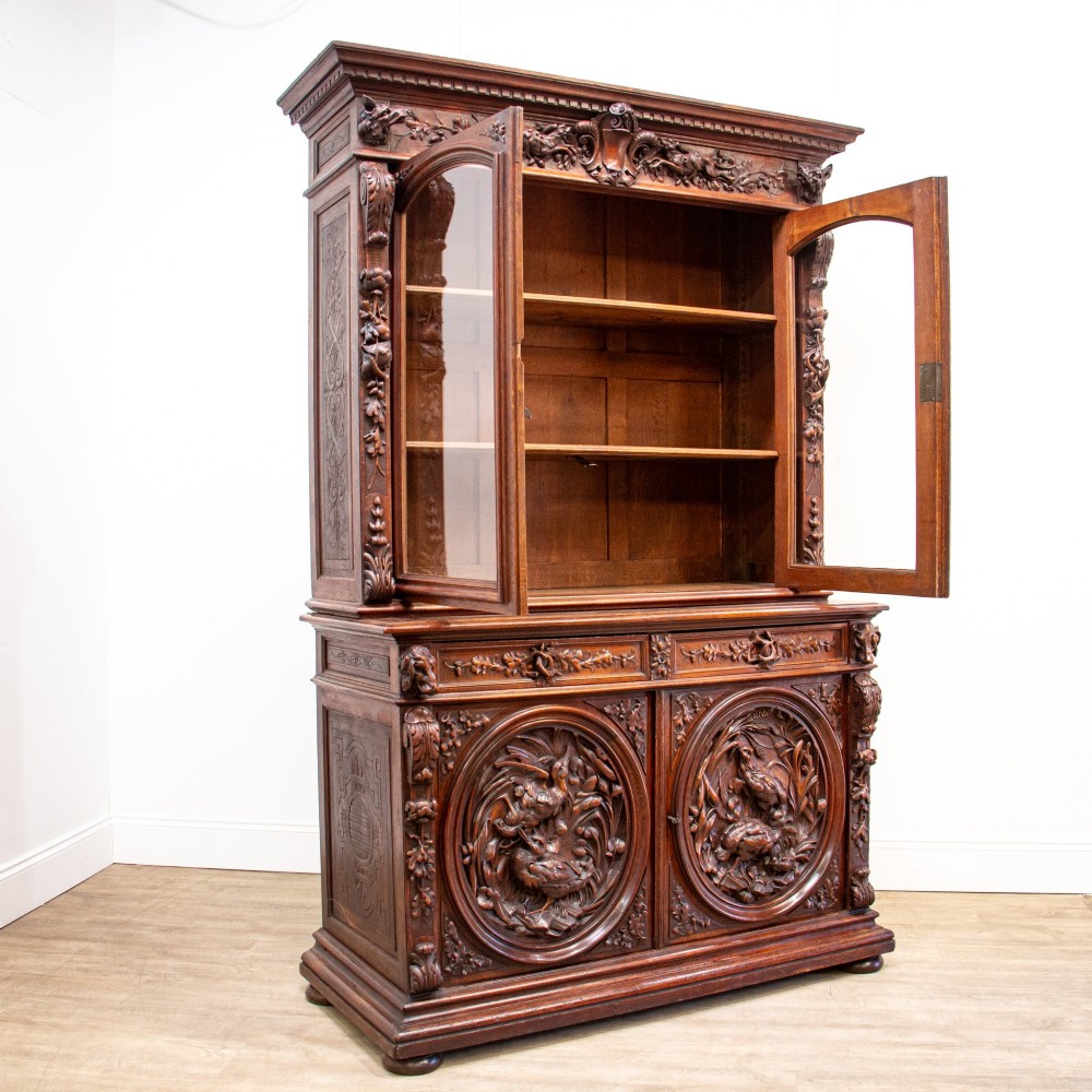 A 19th-century French dark oak two-tier hunting cabinet featuring glazed upper doors and deeply carved lower panels depicting game birds. View X