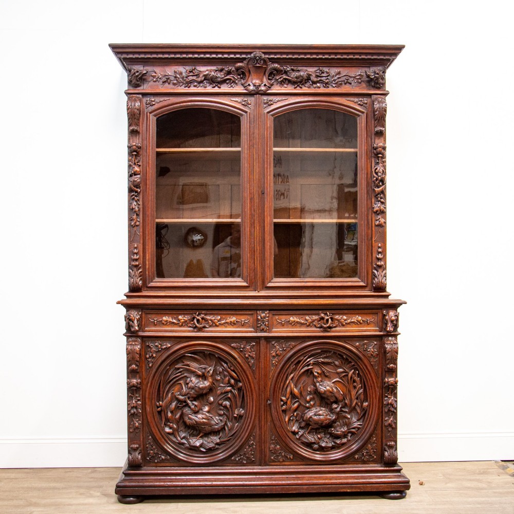 A 19th-century French dark oak two-tier hunting cabinet featuring glazed upper doors and deeply carved lower panels depicting game birds. View XI