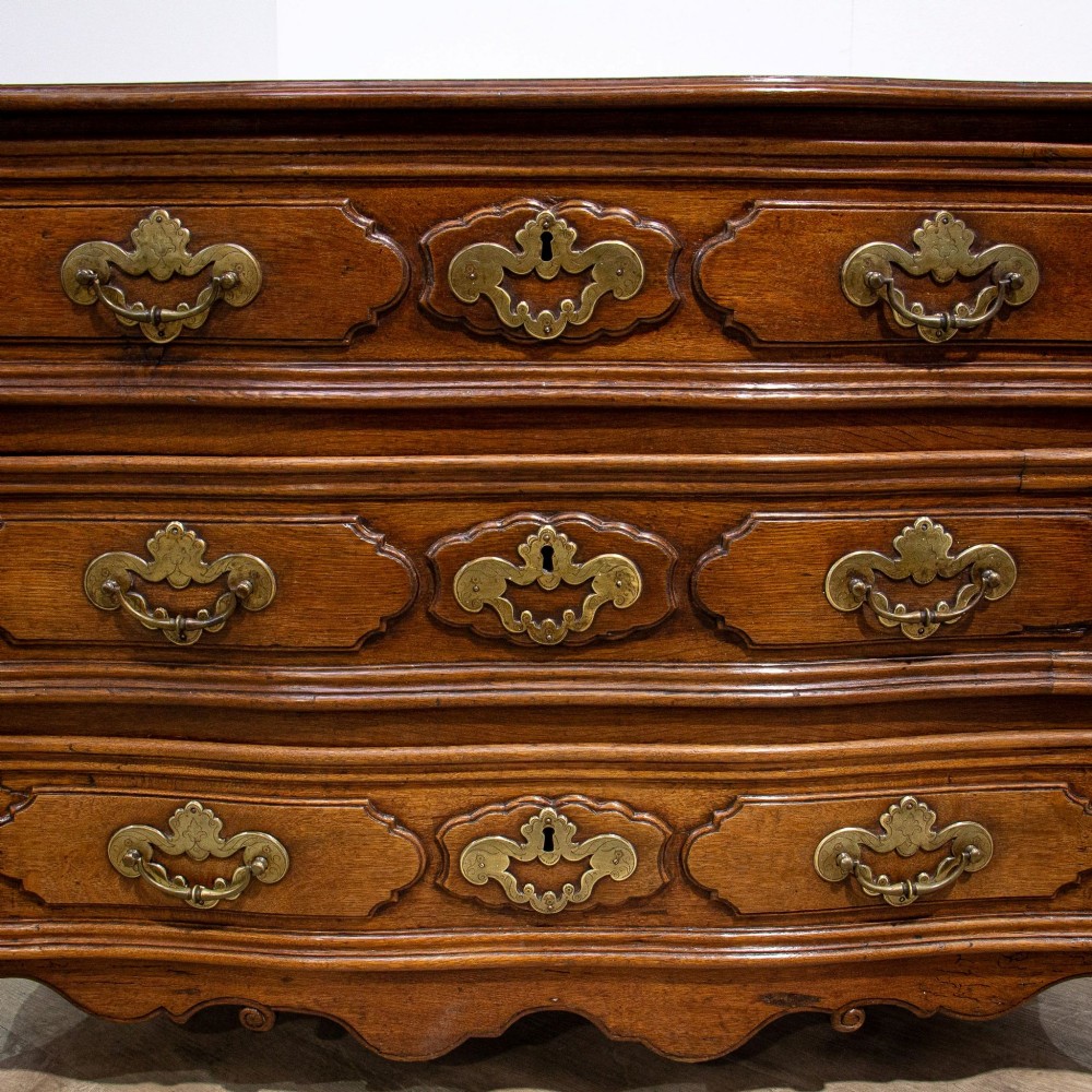 An 18th-century French Louis XV oak commode featuring three serpentine drawers with carved moulded panels, ornate brass handles, and carved cabriole legs. View V