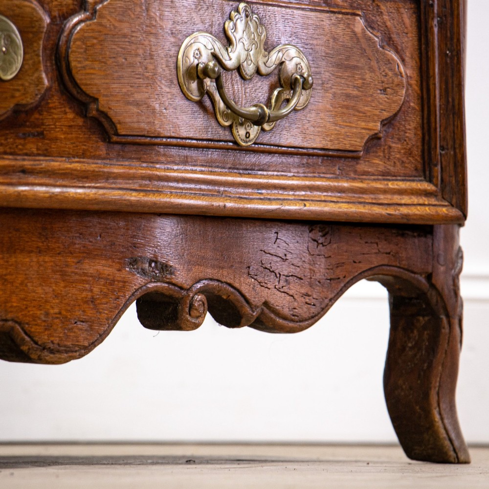 An 18th-century French Louis XV oak commode featuring three serpentine drawers with carved moulded panels, ornate brass handles, and carved cabriole legs. View VI