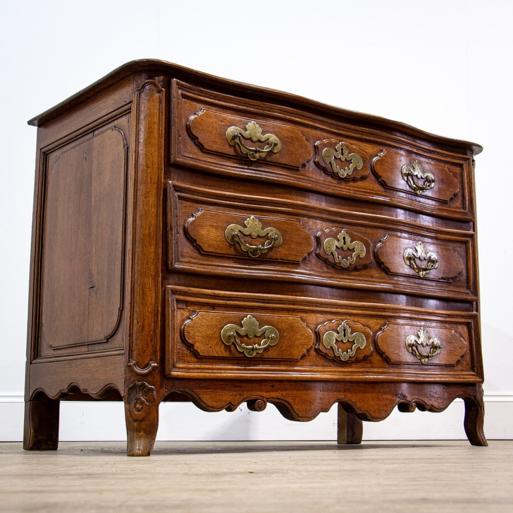 An 18th-century French Louis XV oak commode featuring three serpentine drawers with carved moulded panels, ornate brass handles, and carved cabriole legs. View VIII