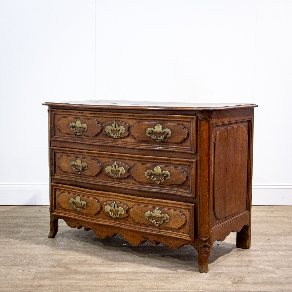 An 18th-century French Louis XV oak commode featuring three serpentine drawers with carved moulded panels, ornate brass handles, and carved cabriole legs. View X