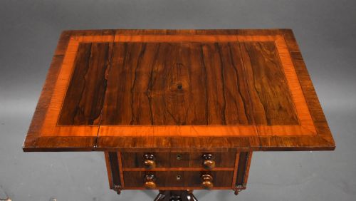 fig 2. A Regency mahogany work table featuring drop leaves, two drawers with round wooden knobs, a turned central pedestal column, and four splayed legs with brass castors.