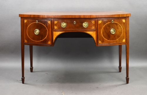 fig 1. A Georgian mahogany bowfront sideboard featuring satinwood oval inlay panels, brass ring handles, and tapered square legs.