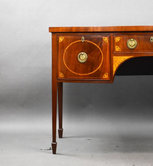 fig 2. A Georgian mahogany bowfront sideboard featuring satinwood oval inlay panels, brass ring handles, and tapered square legs.
