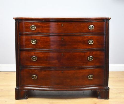 fig 1. An 18th-century mahogany serpentine chest of drawers featuring four graduated drawers with oval brass handles and reeded side columns on bracket feet.