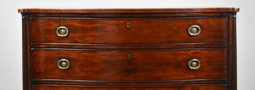 fig 2. An 18th-century mahogany serpentine chest of drawers featuring four graduated drawers with oval brass handles and reeded side columns on bracket feet.