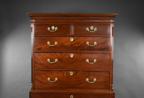 fig 1. A George III mahogany chest on chest featuring multiple stacked drawers with flame mahogany veneer, brass handles, and bracket feet.
