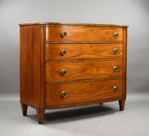 fig 1. A Regency period bowfront chest of four graduated drawers constructed from golden satinwood with crossbanded borders and turned brass knobs.