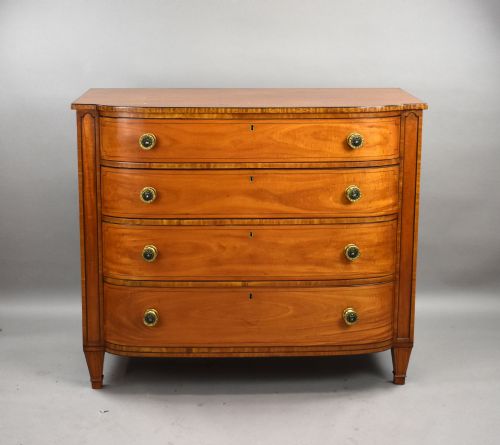 fig 2. A Regency period bowfront chest of four graduated drawers constructed from golden satinwood with crossbanded borders and turned brass knobs.