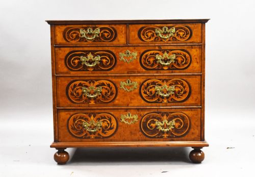 fig 1. A William and Mary burr walnut chest featuring intricate dark marquetry inlay panels, brass swing handles, and turned bun feet.