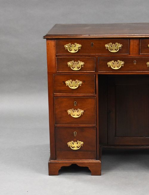 fig 2. A George III mahogany kneehole desk featuring a flat rectangular top, brass swan-neck handles on multiple drawers, a central recessed cupboard, and bracket feet.