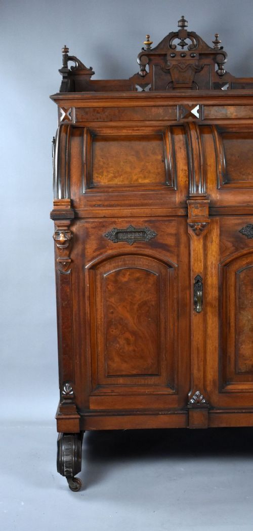 A Victorian walnut Wooton secretary desk featuring carved cresting, curved upper doors, panelling, brass mail slots, and carved feet on castors. View XV
