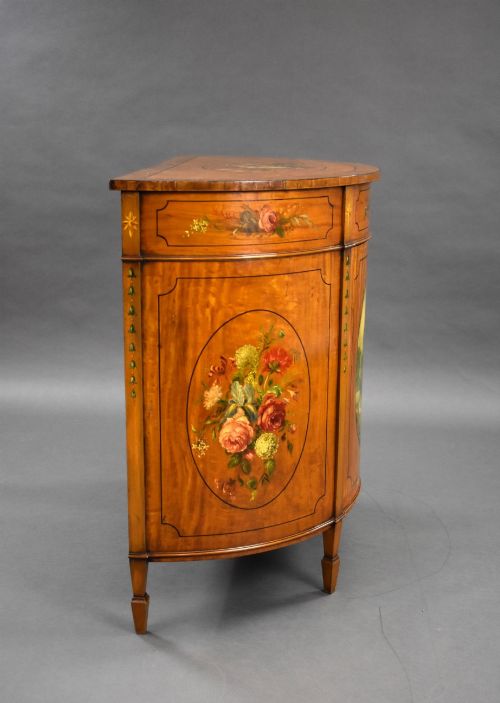 fig 2. An Edwardian demi-lune satinwood cabinet featuring hand-painted floral and landscape medallions on two doors and tapered legs.