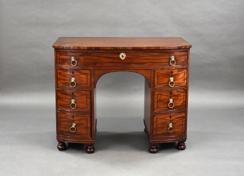 fig 1. An antique Regency flame mahogany kneehole dressing chest with seven drawers, brass lion mask ring handles, and turned feet.