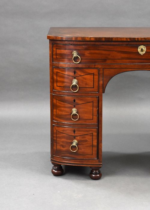 fig 2. An antique Regency flame mahogany kneehole dressing chest with seven drawers, brass lion mask ring handles, and turned feet.